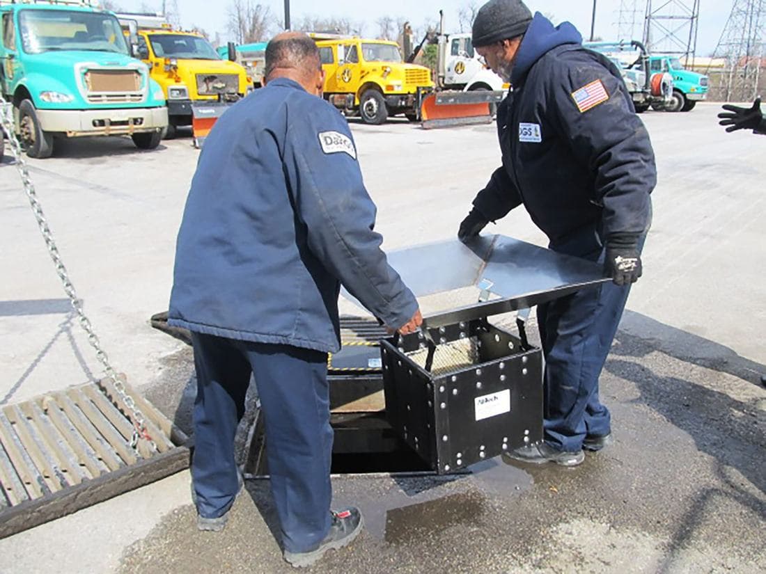 Two crew members setting a filter insert into an open catch basin