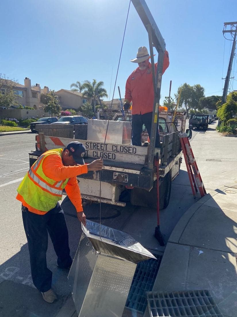 Crew lowering a stainless filter box into a curb inlet
